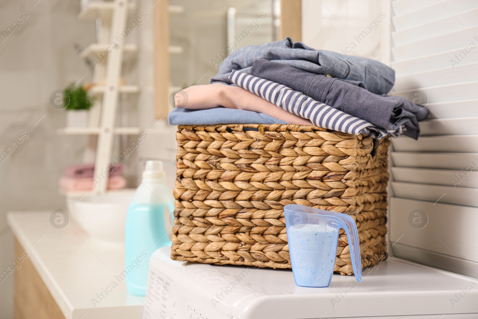Photo of Wicker basket with laundry and detergent on washing machine in bathroom. Space for text