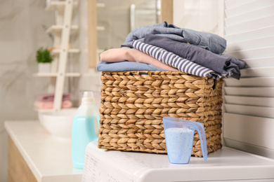 Wicker basket with laundry and detergent on washing machine in bathroom. Space for text