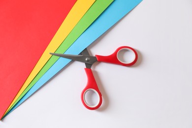 Photo of Red scissors and color sheets of paper on white background, flat lay