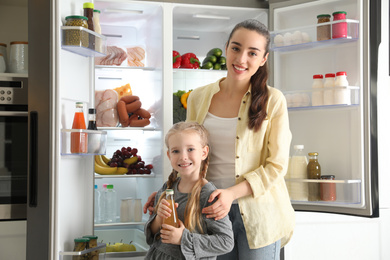 Photo of Young mother with daughter near open refrigerator in kitchen