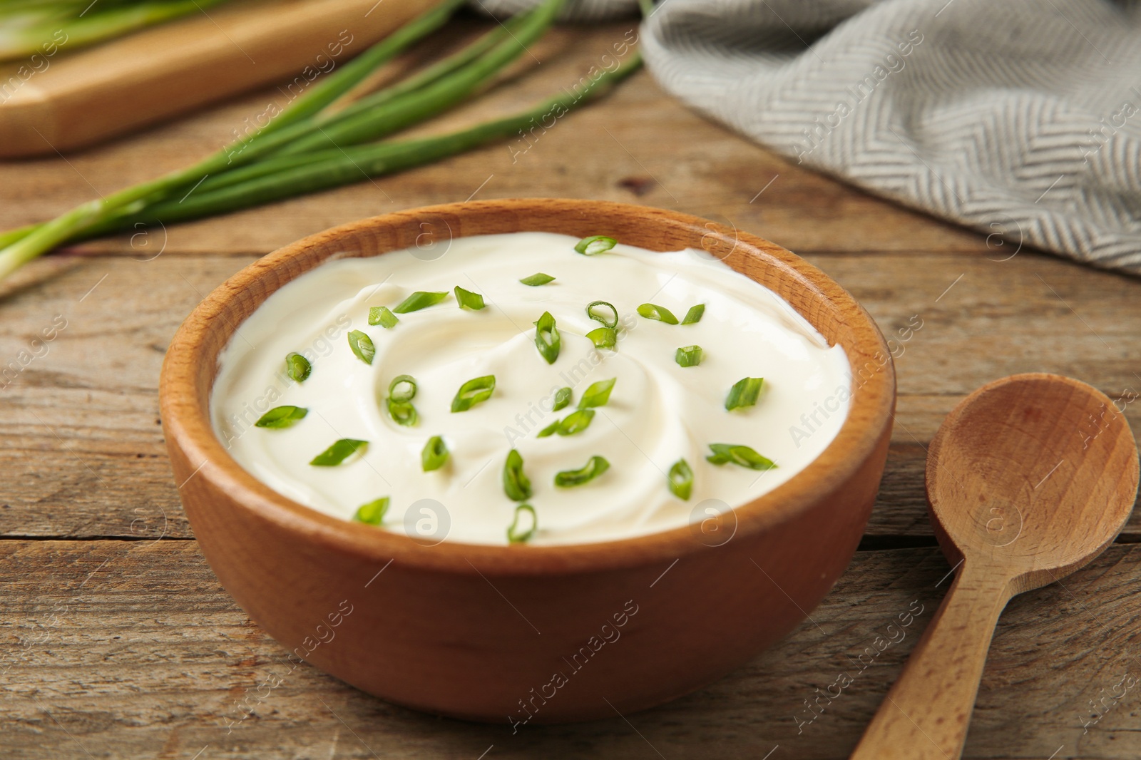 Photo of Bowl of fresh sour cream with green onion and spoon on wooden table