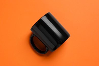 Photo of One black ceramic mug on orange background, top view