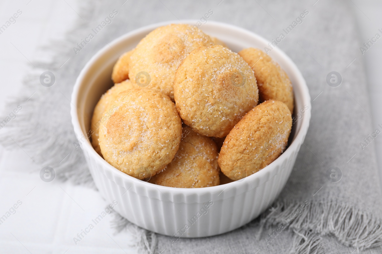 Photo of Tasty sugar cookies in bowl on white tiled table, closeup