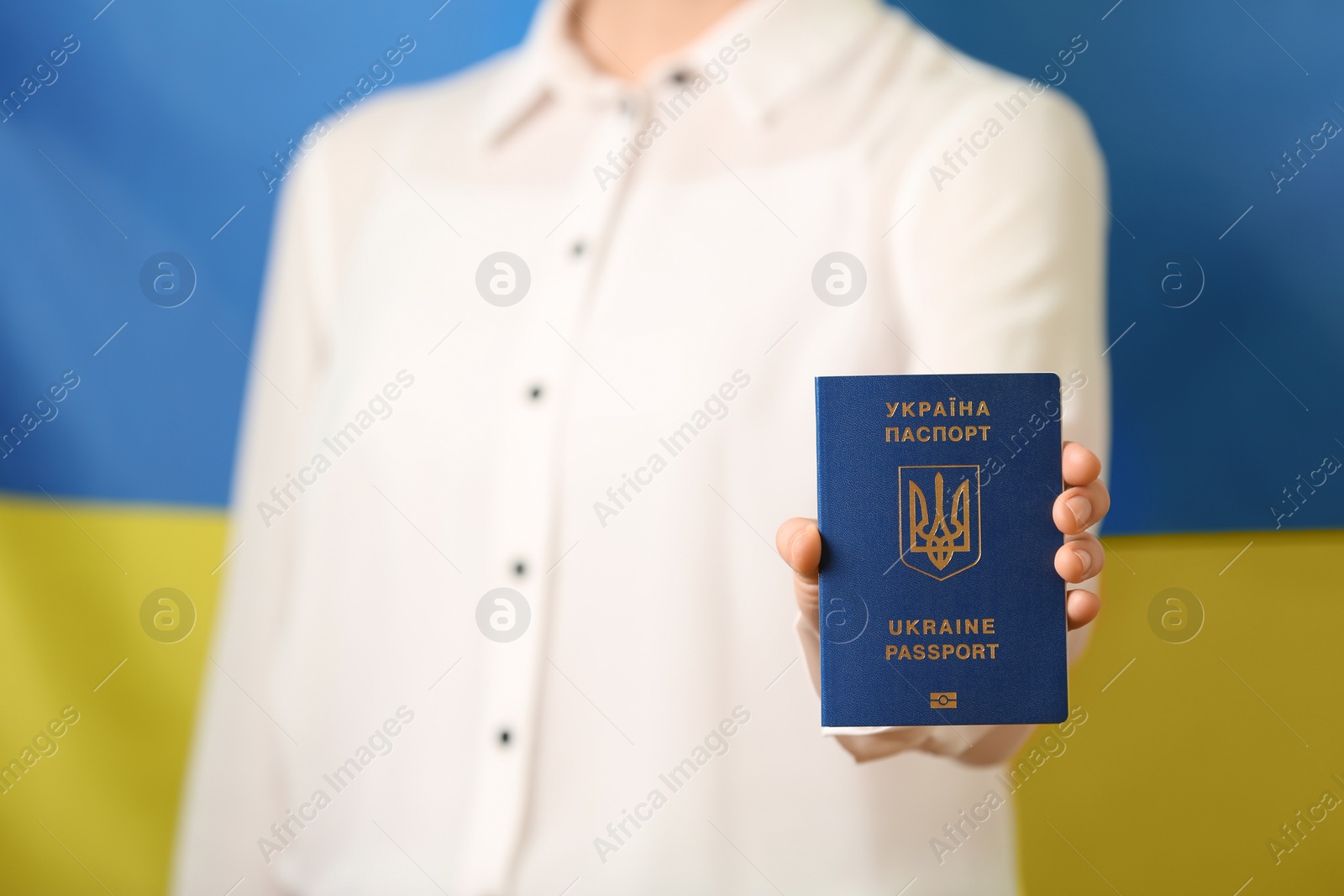 Photo of Woman holding Ukrainian travel passport against national flag, closeup. International relationships