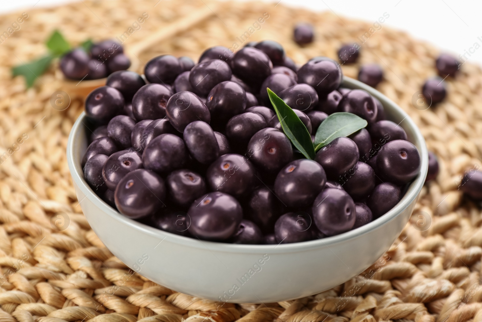 Photo of Tasty acai berries in bowl on wicker mat, closeup