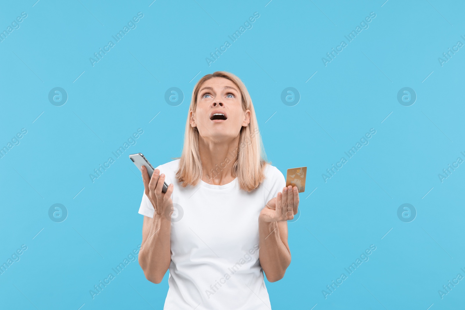Photo of Emotional woman with credit card and smartphone on light blue background. Be careful - fraud