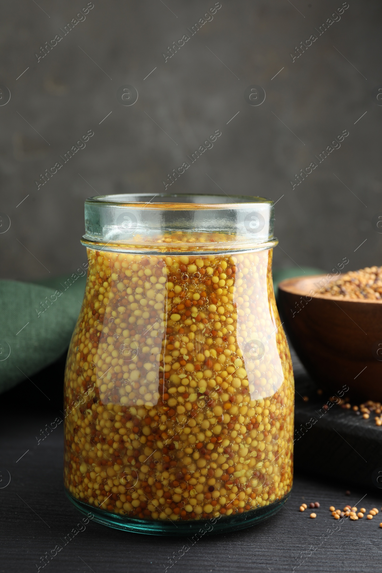 Photo of Whole grain mustard in jar and dry seeds on black wooden table