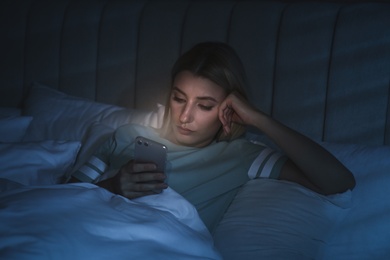 Young woman using smartphone in bed at night. Nomophobia and sleeping disorder problem