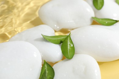 Photo of Spa stones and green leaves in water on yellow background, closeup