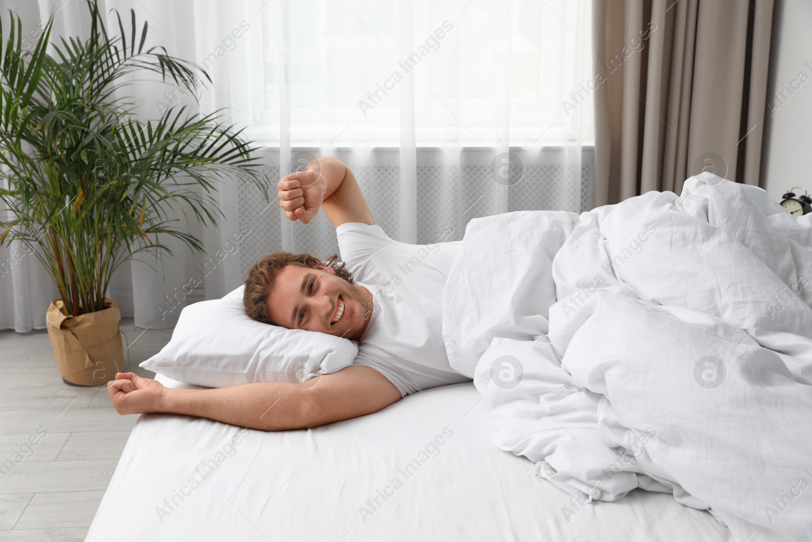 Photo of Sleepy young man stretching while lying under blanket in morning. Bedtime