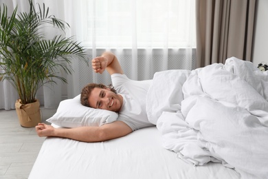 Sleepy young man stretching while lying under blanket in morning. Bedtime