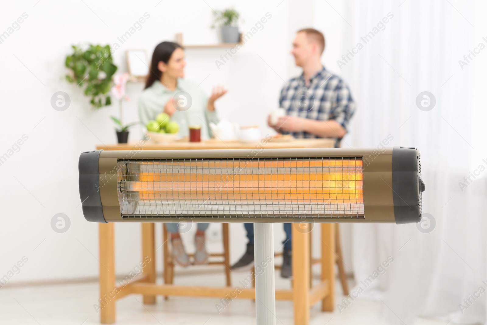 Photo of Couple spending time in room with modern electric infrared heater, focus on appliance