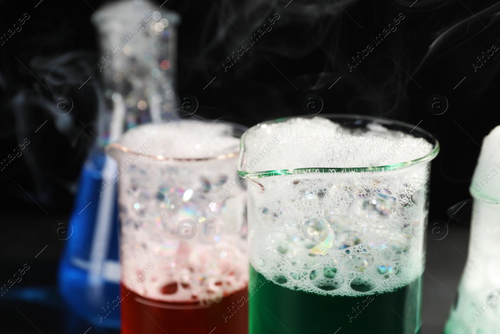 Photo of Laboratory glassware with colorful liquids and steam on black background, closeup. Chemical reaction