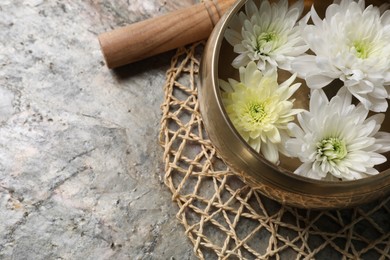 Photo of Tibetan singing bowl with water, beautiful chrysanthemum flowers and mallet on table, above view. Space for text