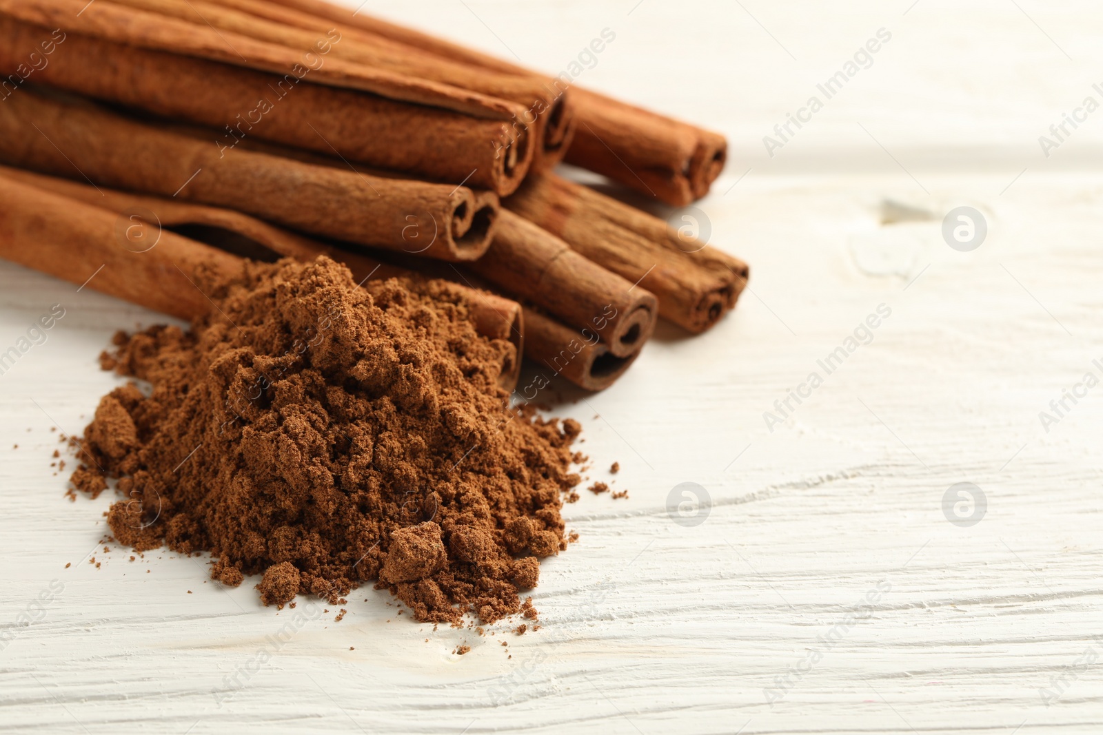Photo of Aromatic cinnamon powder and sticks on white wooden table, closeup. Space for text