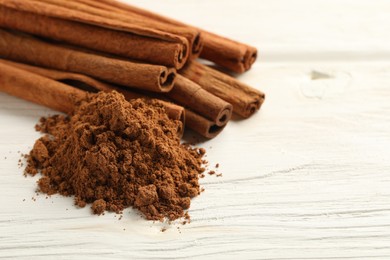 Photo of Aromatic cinnamon powder and sticks on white wooden table, closeup. Space for text