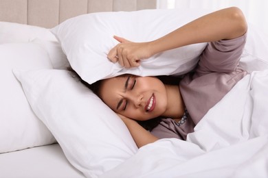 Unhappy African American woman covering ears with pillows in bed at home