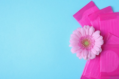 Packed menstrual pads and flower on color background, flat lay with space for text. Gynecological care