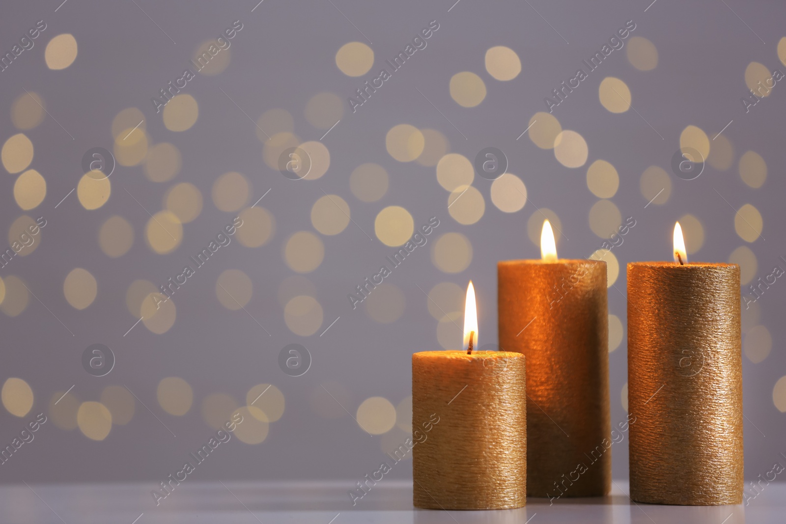 Photo of Burning gold candles on table against blurred lights. Space for text