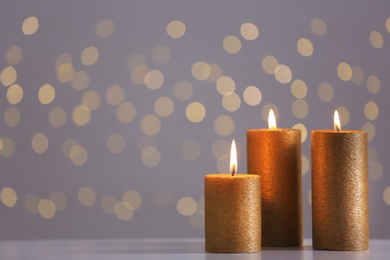 Photo of Burning gold candles on table against blurred lights. Space for text