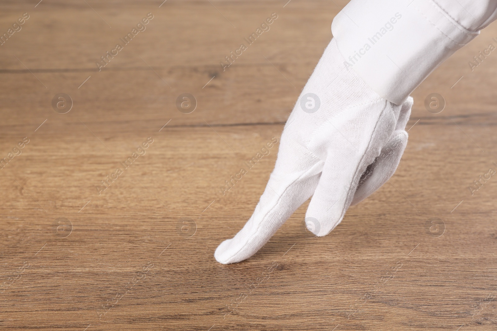 Photo of Person in white glove checking cleanliness of wooden  table, closeup. Space for text