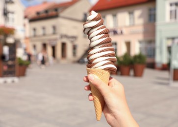 Woman holding delicious ice cream cone in city, closeup