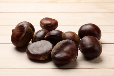 Sweet fresh edible chestnuts on light wooden table, closeup