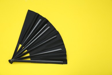Photo of Stylish black hand fan on yellow background, top view. Space for text