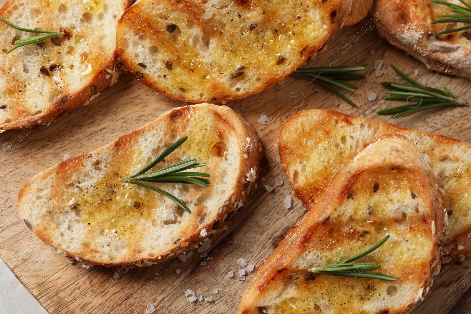 Photo of Tasty bruschettas with oil and rosemary on wooden board, top view