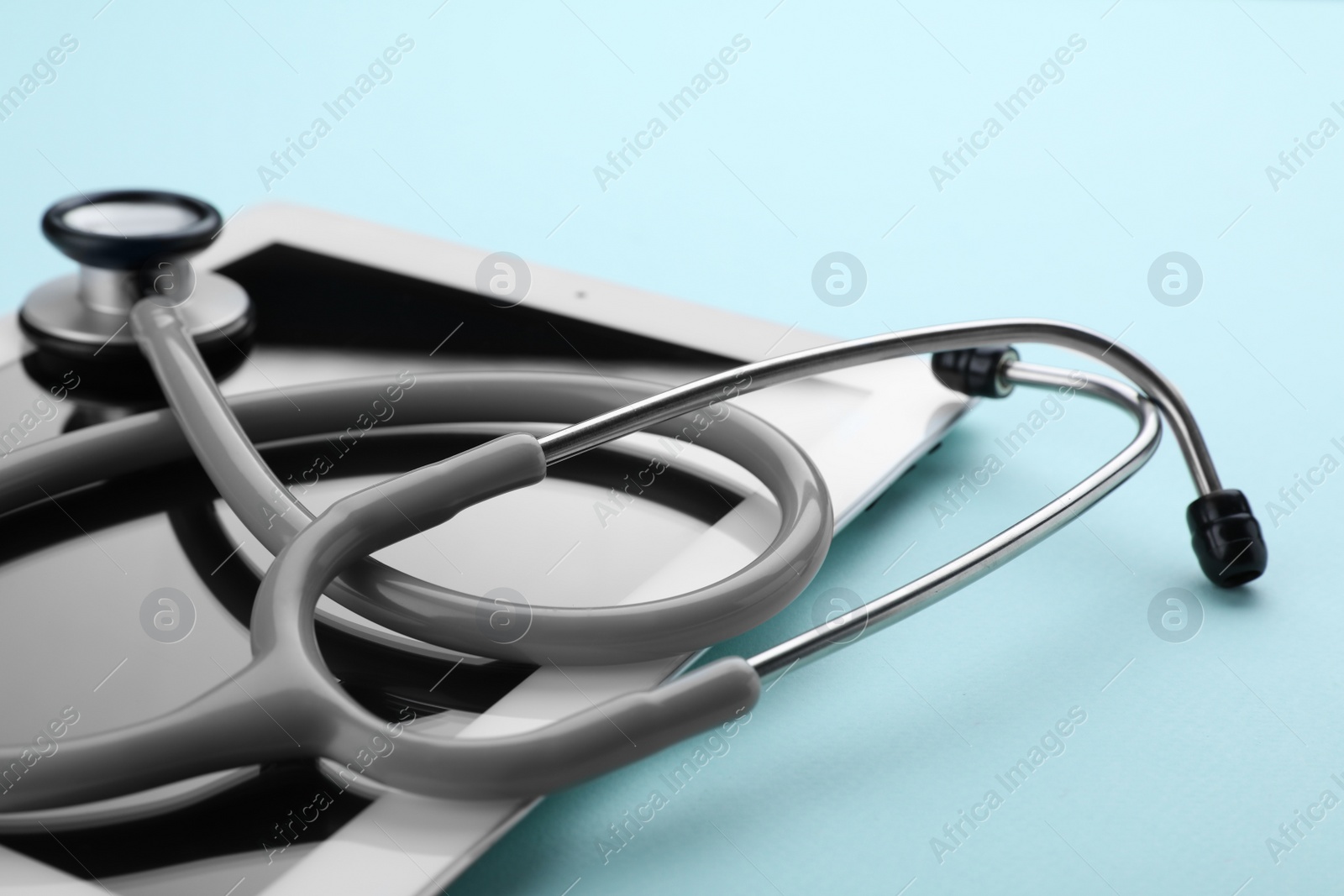 Photo of Computer tablet and stethoscope on turquoise background, closeup