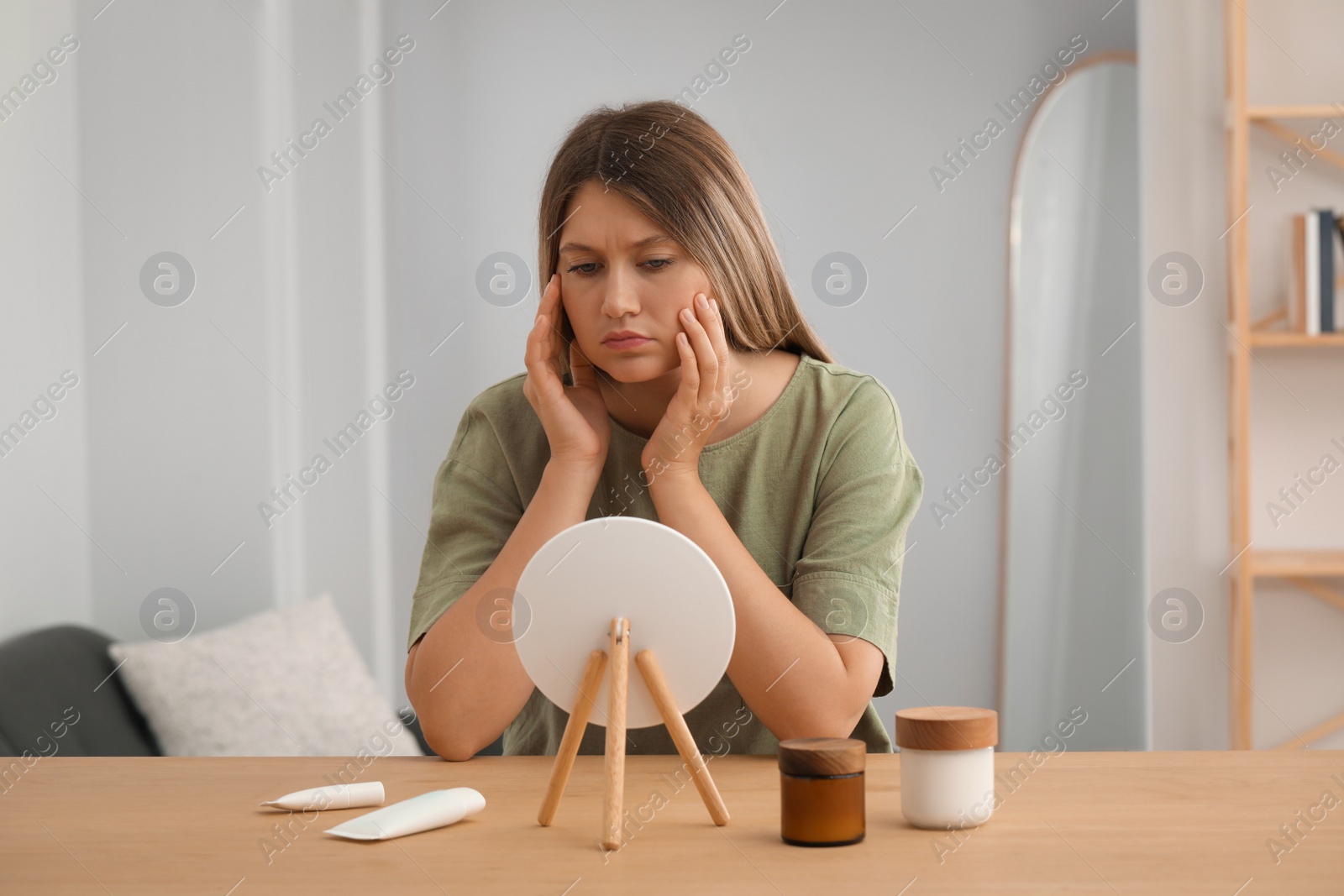 Photo of Sleep deprived young woman looking at herself in mirror indoors