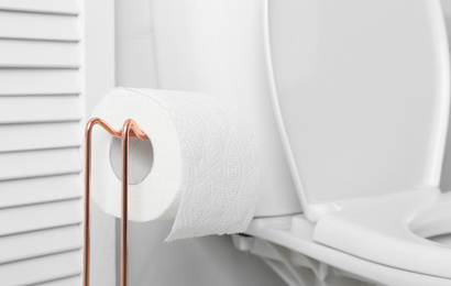Photo of Holder with paper roll near toilet bowl in bathroom