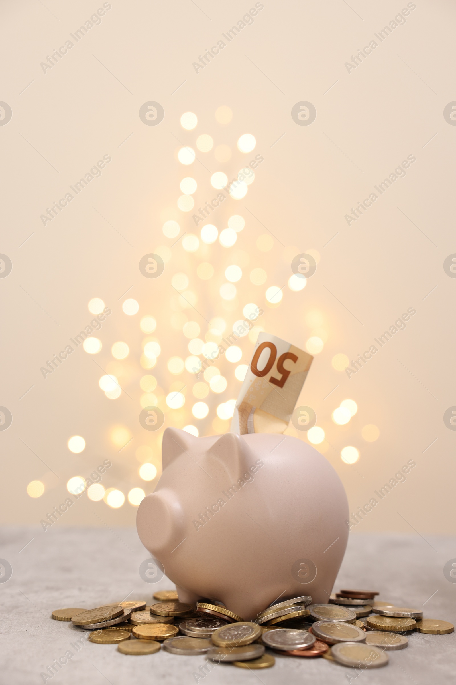 Photo of Piggy bank with euro banknote and coins on grey table against blurred lights, space for text