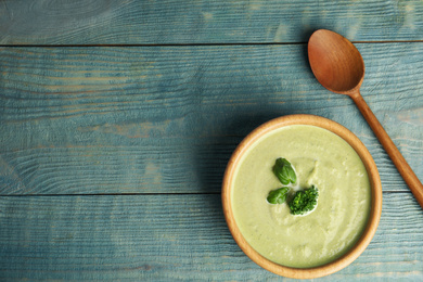 Photo of Delicious broccoli cream soup served on blue wooden table, flat lay. Space for text