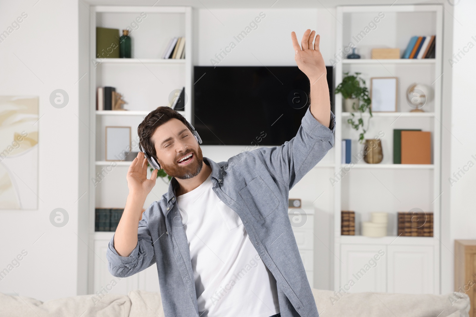 Photo of Emotional man dancing while listening music with headphones at home