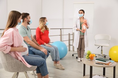 Photo of Pregnant women, man and doctor with protective masks at courses for expectant parents indoors