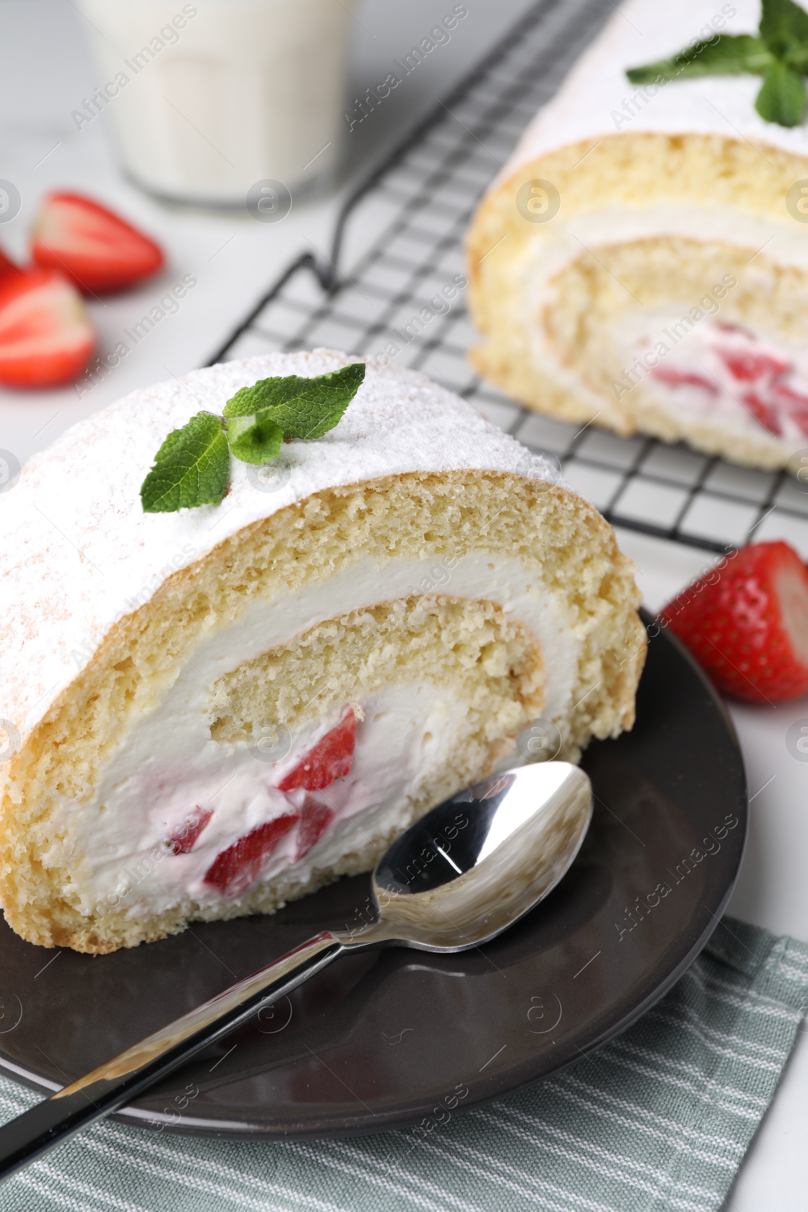 Photo of Slice of delicious sponge cake roll with strawberries and cream served on white table, closeup