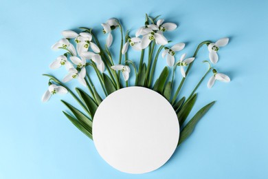 Beautiful snowdrops and paper card on light blue background, flat lay. Space for text