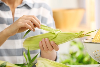 Photo of Woman husking corn at table, focus on hands