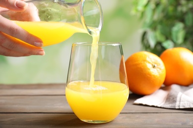 Photo of Woman pouring fresh orange juice into glass on wooden table, closeup