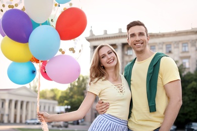 Young couple with colorful balloons outdoors on sunny day