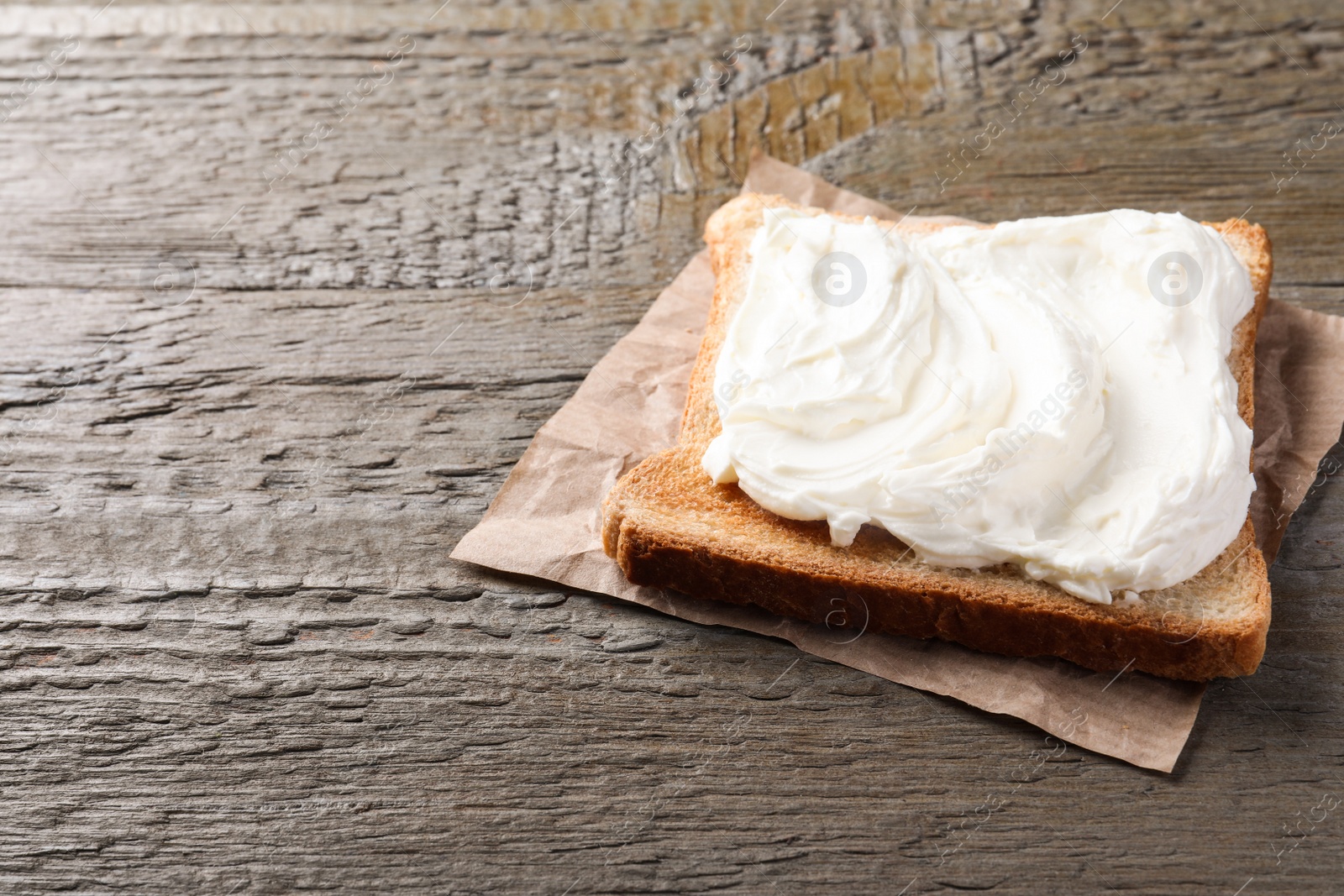 Photo of Slice of bread with tasty cream cheese on wooden table, space for text