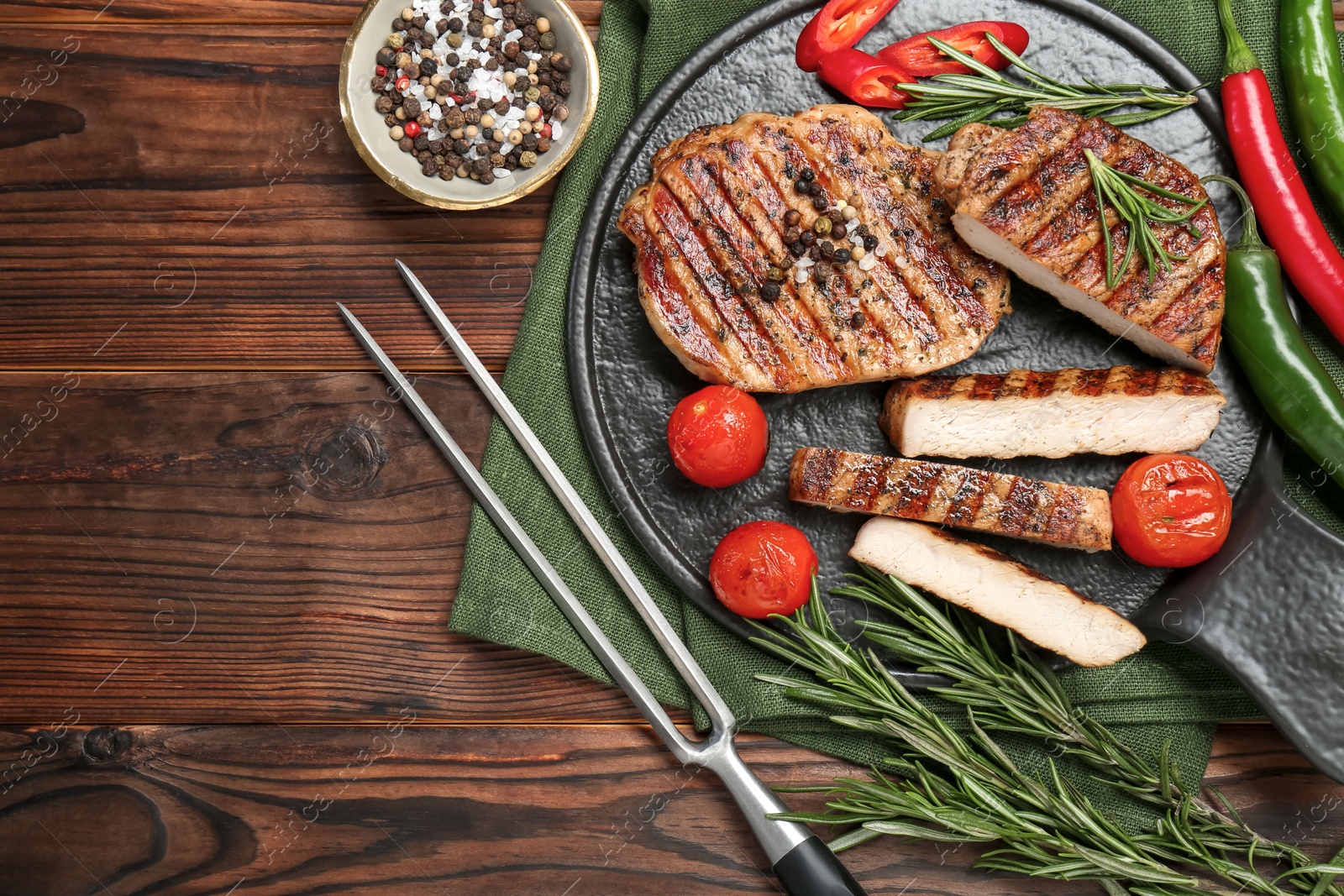 Photo of Grilled pork steaks with rosemary, spices, vegetables and carving fork on wooden table, top view. Space for text