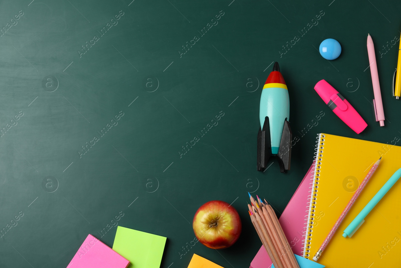 Photo of Bright toy rocket and school supplies on chalkboard, flat lay. Space for text