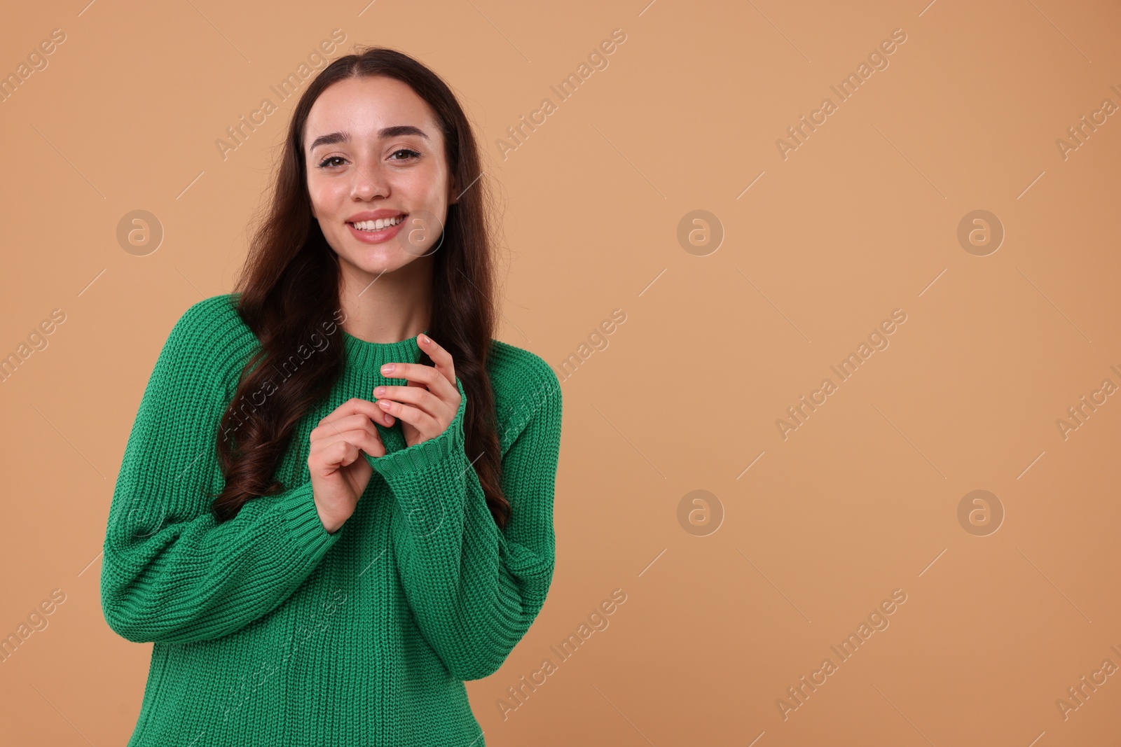 Photo of Beautiful young woman in stylish warm sweater on beige background, space for text