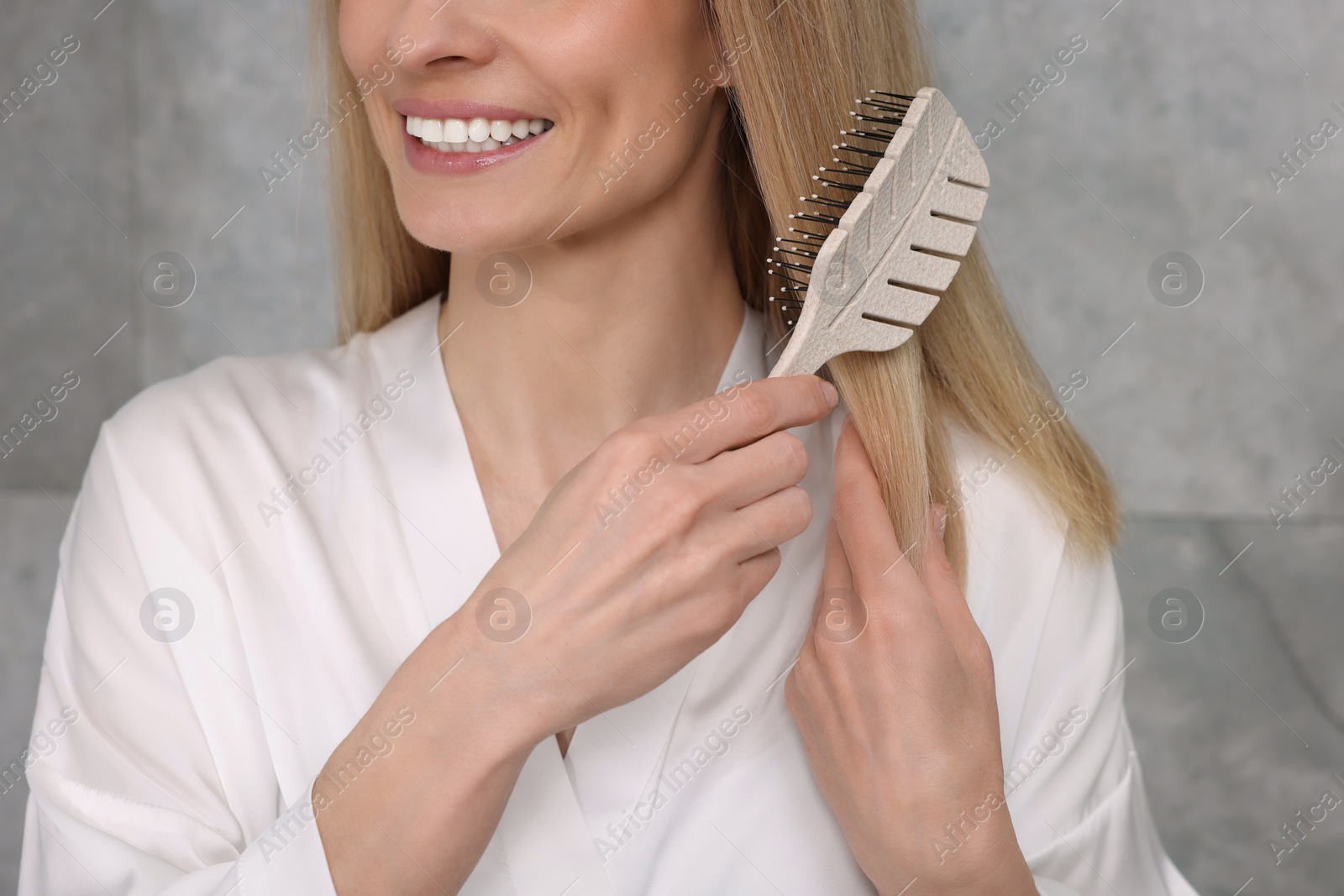 Photo of Woman in white robe brushing her hair indoors, closeup