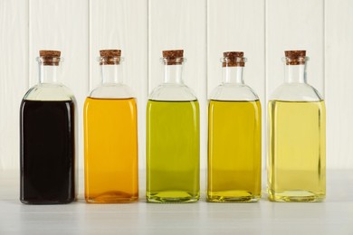 Photo of Vegetable fats. Different cooking oils in glass bottles on white wooden table