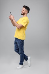 Happy young man using smartphone on grey background