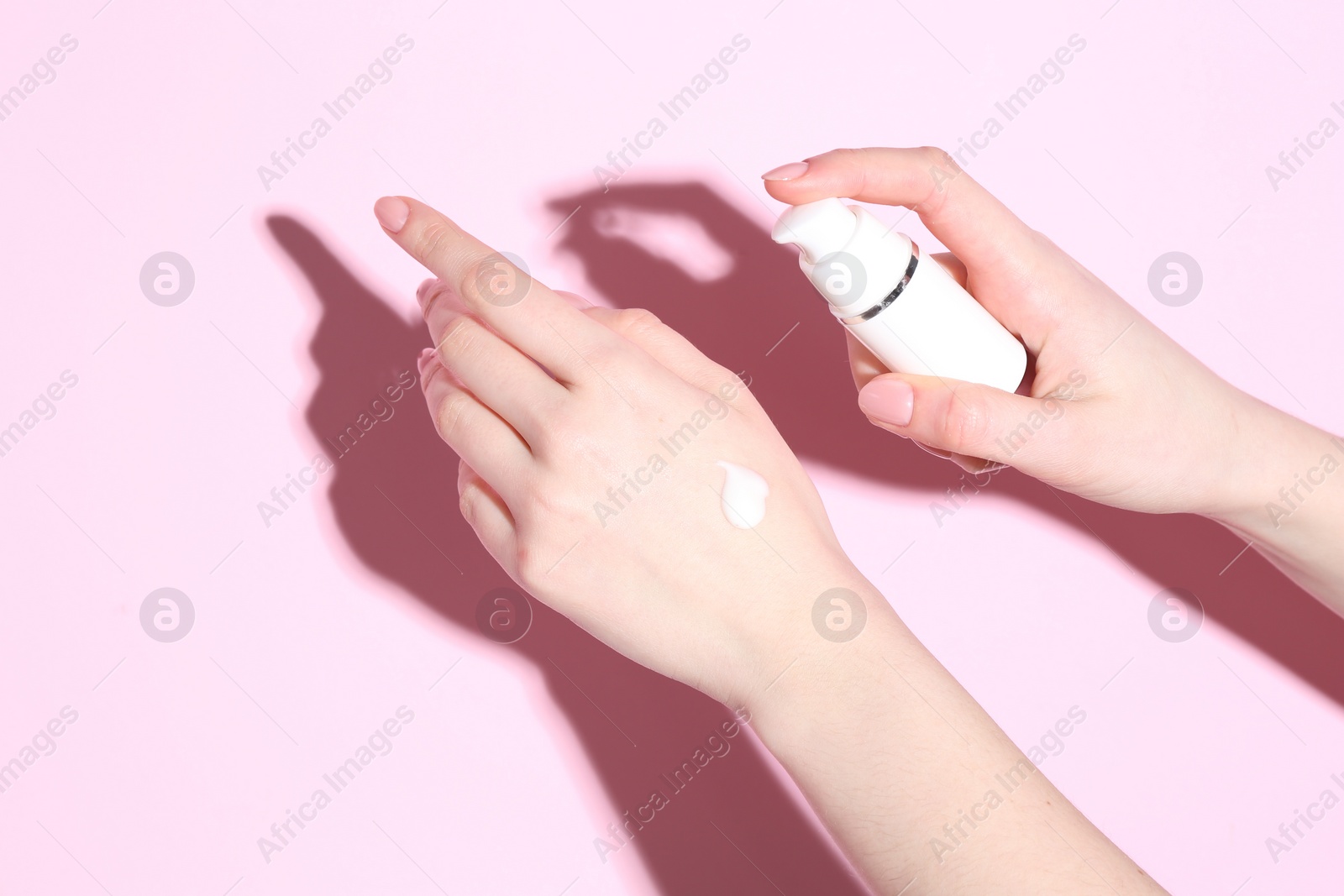 Photo of Woman applying cream on her hand against pink background, closeup