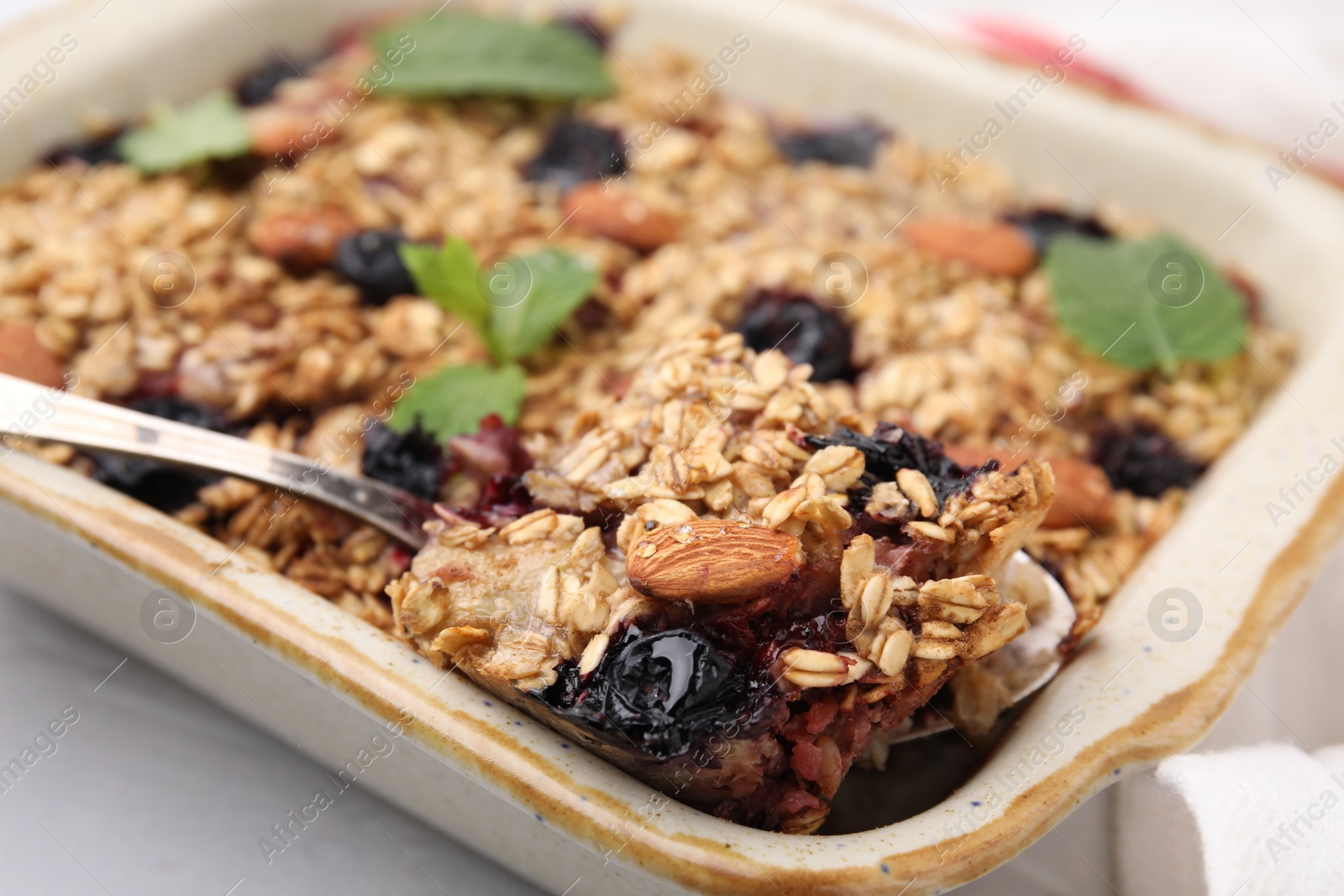 Photo of Tasty baked oatmeal with berries and almonds in baking tray on white table, closeup